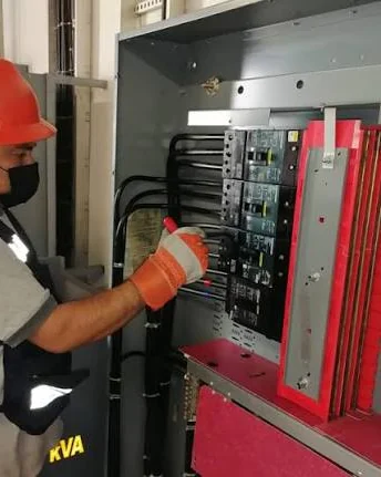 Operador con casco y guantes dieléctricos accionando las protecciones de un tablero de fuerza.